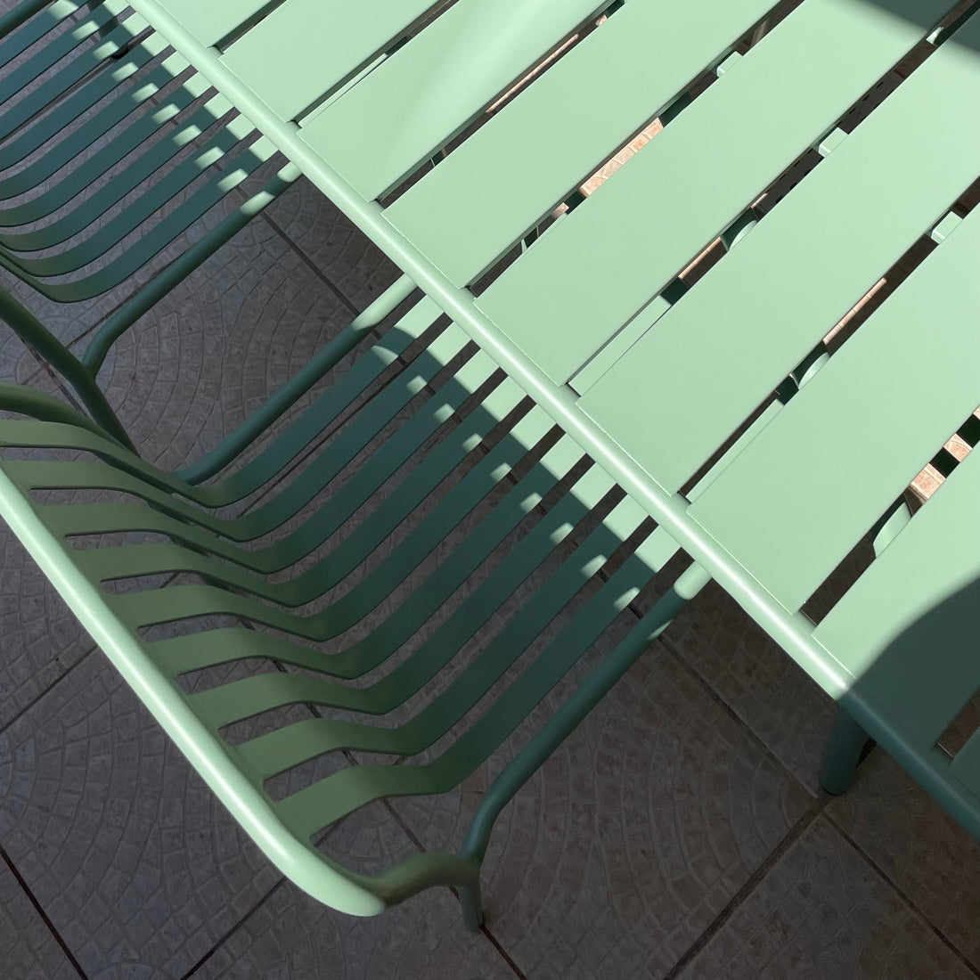 Table de jardin en métal vert à lattes avec chaises assorties sur terrasse, lumière naturelle et plante en pot au centre, ambiance extérieure contemporaine – Rendez-vous Déco