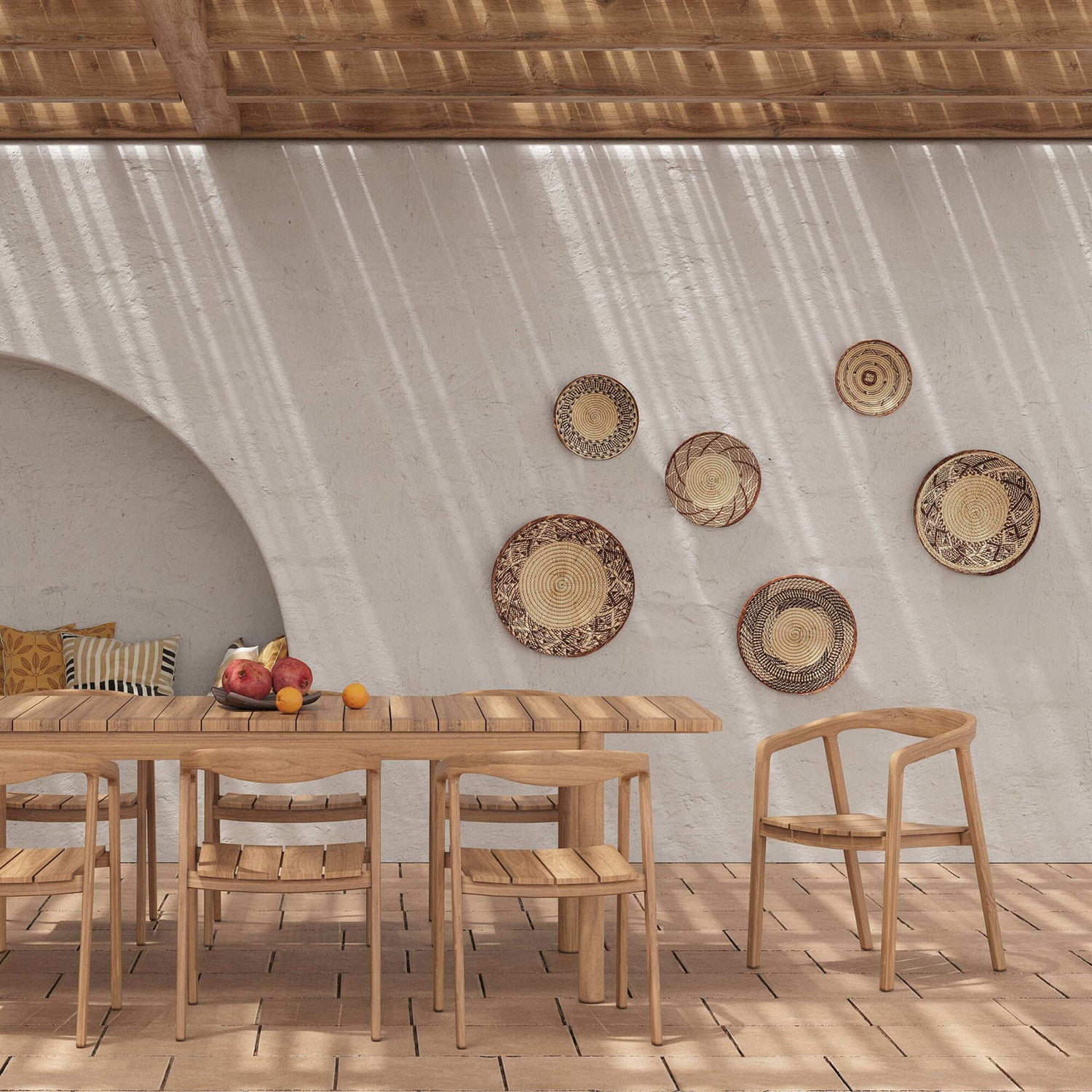 Salle à manger avec table et chaises en bois clair, ambiance méditerranéenne lumineuse, mur blanc texturé avec niche arrondie et décor mural en fibres naturelles, sol en terre cuite, Rendez-vous Déco