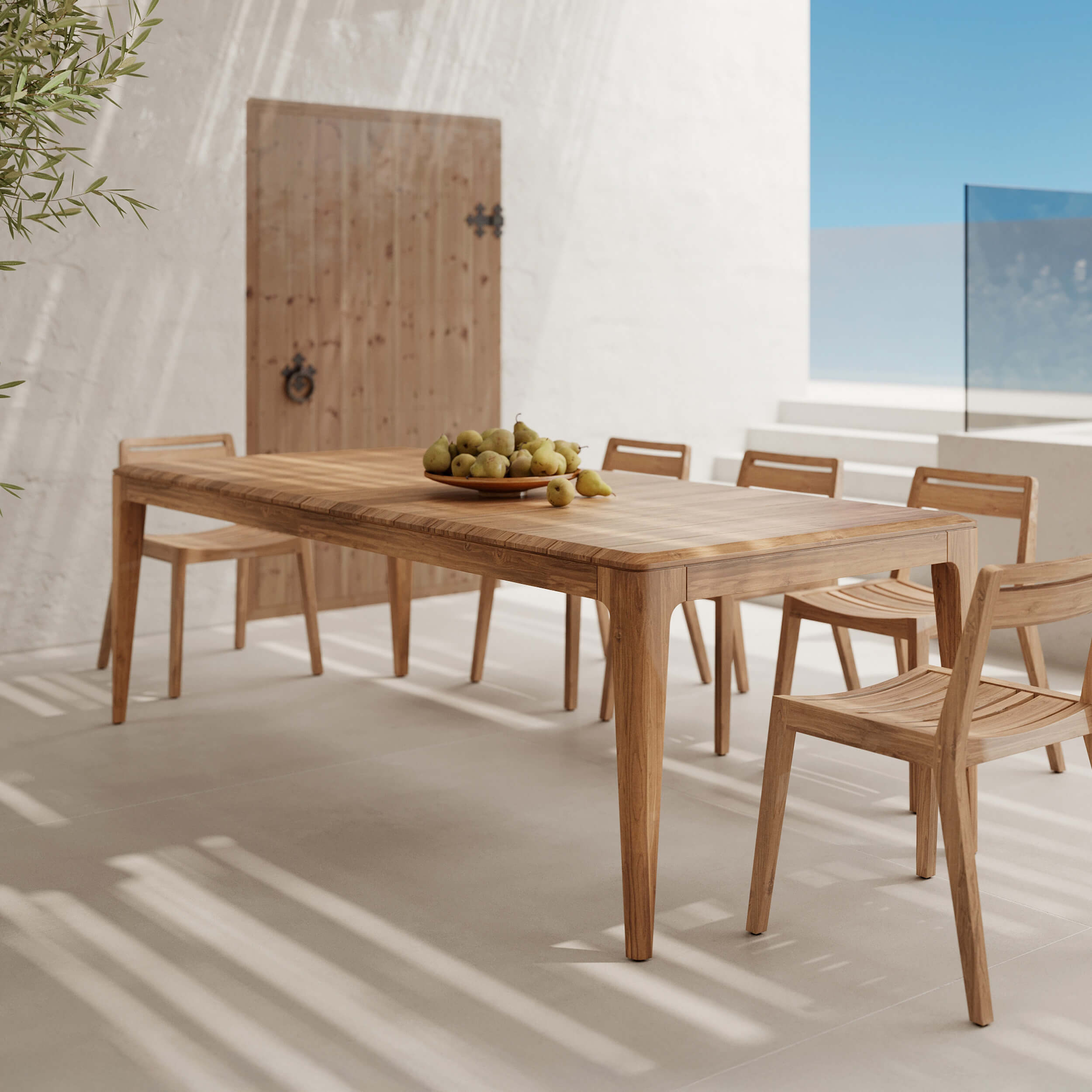 Table à manger rectangulaire en bois massif avec chaises assorties, ambiance méditerranéenne lumineuse, mur blanc texturé et porte en bois, lumière naturelle avec ombres graphiques au sol, Rendez-vous Déco