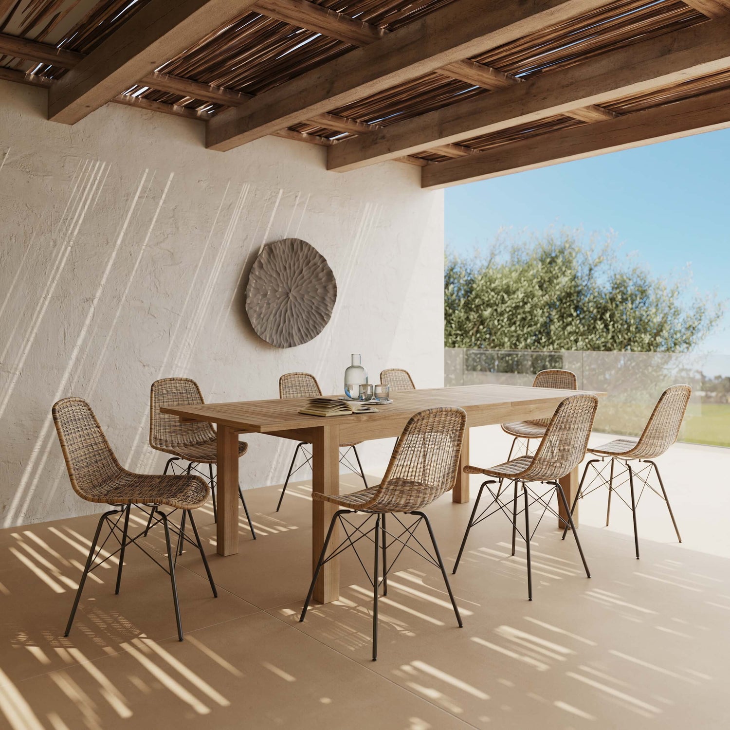 Table salle à manger bois massif entourée de chaises rotin, sous pergola lumineuse aux poutres apparentes – Rendez-vous Déco
